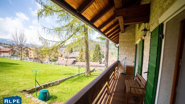 A wooden balcony with a bench, a green bucket, and a view of a green field and buildings in the background. - Villa Gentilini, nature & comfort (Serrada)