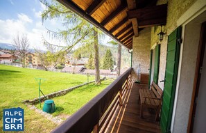 A wooden balcony with a bench, a green bucket, and a view of a green field and buildings in the background. - Villa Gentilini, nature & comfort (Serrada)