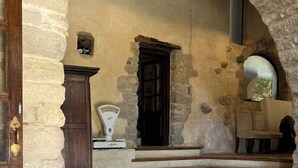 Un interior de paredes de piedra con una puerta de madera, una balanza y un banco.