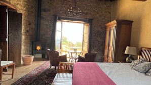 Una habitación rústica con una cama grande, muebles de madera, una chimenea y vistas a través de una ventana abierta.