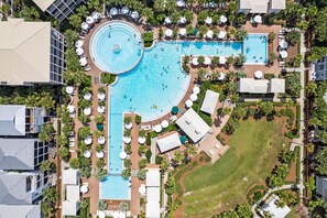Vista aérea de um resort com uma grande piscina central, várias piscinas menores e espreguiçadeiras dispostas ao redor das piscinas.