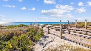 A wooden boardwalk leading to a beach with clear blue sky and ocean views. - Luxury Coastal Living • Breezy Partially Screened Porch & Lagoon Pool Access (Seacrest Beach)