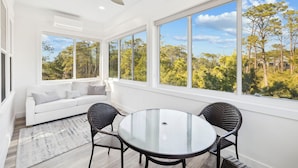 A bright, modern room with a white ceiling, large windows, a white sofa, a glass table, and two wicker chairs. - Luxury Coastal Living • Breezy Partially Screened Porch & Lagoon Pool Access (Seacrest Beach)