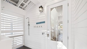 A white exterior with a glass door, a metal sign reading "BEACH HOUSE", and a metal towel rack. - Luxury Coastal Living • Breezy Partially Screened Porch & Lagoon Pool Access (Seacrest Beach)