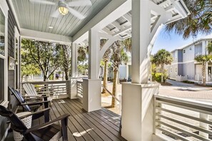 Relax in a serene outdoor space with Adirondack chairs and a ceiling fan, surrounded by palm trees and a residential building.