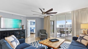 A modern living room with a flat-screen TV, a ceiling fan, a wooden coffee table, and a sofa with starfish pillows. - Destin West Heron 607 ~ Beach Paradise ~ All the Upgrades ~ Overlooking the Lazy River (Fort Walton Beach)