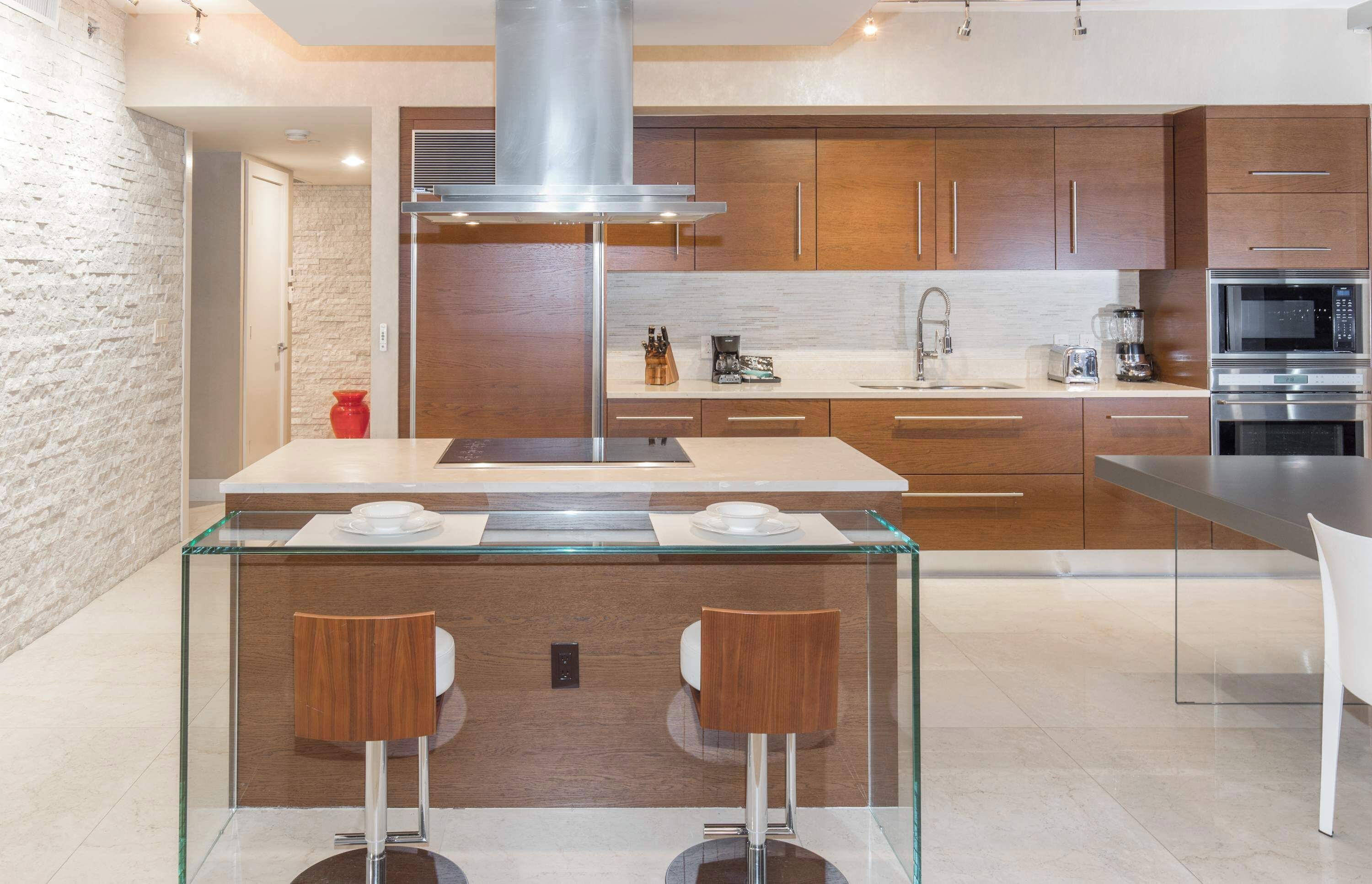 A modern kitchen with wooden cabinets, stainless steel appliances, and a glass island with two bar stools.
