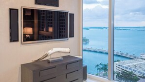 A modern room with a large window overlooking a marina and a bridge, a dark wooden dresser, and a mounted television. - Prime Brickell Suite | Walk to City Center (Miami)