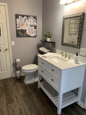 Et badeværelse med en hvid kommode, et stort spejl, et toilet og et blomsterbillede på væggen.