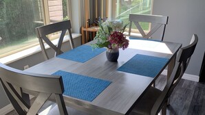 A dining table with blue placemats, surrounded by chairs, in a room with a large window and a 'WELCOME' sign on the wall. - Beaver Lake Get-a-Way          Great Location--Beautiful View (Rogers)