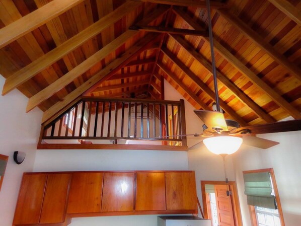 A room with a sloped wooden ceiling, a ceiling fan, and wooden cabinets.