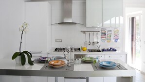 Una cocina moderna con armarios blancos, una isla central con un jarrón de orquídeas blancas y una variedad de platos y utensilios sobre la isla.