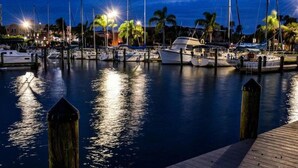 A marina at dusk with boats docked, palm trees, and a wooden dock.