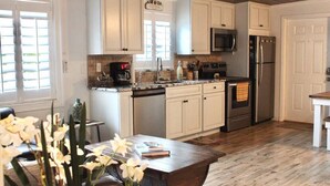 A kitchen with white cabinets, a microwave, a refrigerator, and a coffee maker. There is a wooden table with a vase of flowers.