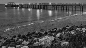 A pier extending into calm waters with a rocky shoreline in the foreground.