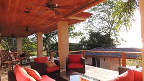An outdoor patio with wicker furniture, red cushions, and a ceiling fan. - Beachfront paradise on Playa Portrero (Potrero)