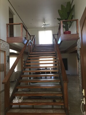 A wooden staircase with a ceiling fan, a potted plant, and a view of the upper floor.
