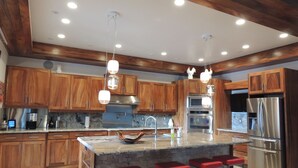 A modern kitchen with wooden cabinets, stainless steel appliances, a granite countertop, and a central island with red bar stools. - Beachfront paradise on Playa Portrero (Potrero)