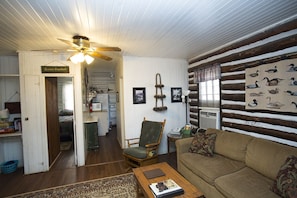 Interior acolhedor de uma cabana com teto de madeira, uma poltrona estofada verde, um sofá marrom e um ventilador de teto.