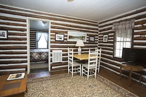 Quarto de cabana de toras com uma mesa de jantar e cadeiras, uma televisão e um tapete estampado.