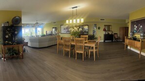 A spacious living room with a dining area, a sofa, and a large window providing a view of the outside. - Luxurious, Newer Oceanfront, Professionally Decorated, Beautiful Condo (Cocoa Beach)