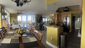 A spacious living area with a dining table set for four, a kitchen with modern appliances, and a balcony with outdoor furniture. - Luxurious, Newer Oceanfront, Professionally Decorated, Beautiful Condo (Cocoa Beach)