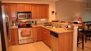Una cocina con armarios de madera, electrodomésticos de acero inoxidable, encimera de granito y un comedor con mesa y sillas.