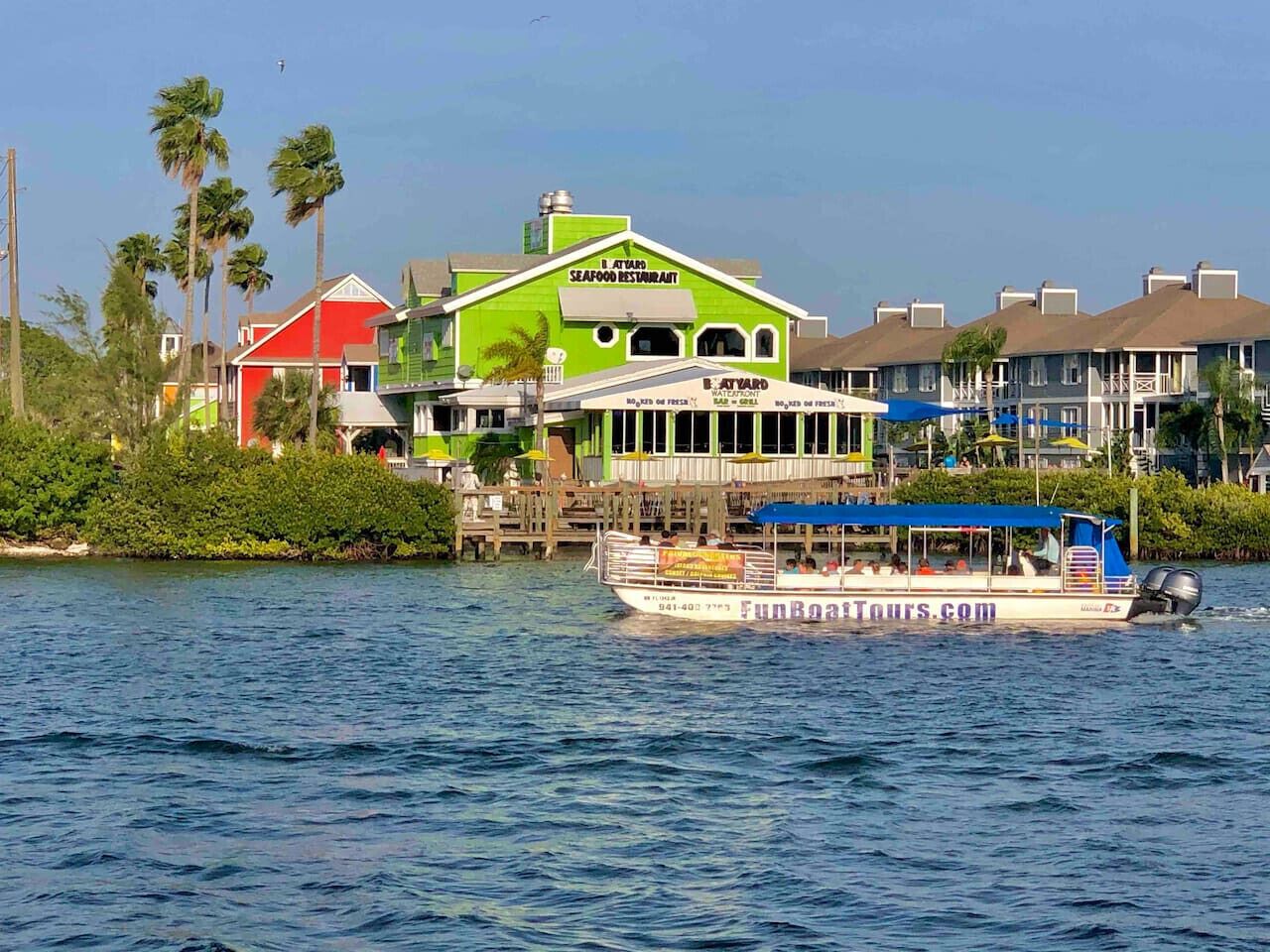 Un restaurant situé au bord de l’eau, avec une façade verdoyante et un bateau amarré à proximité.