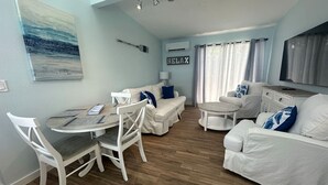 Uma sala de estar moderna com área de jantar, móveis brancos e um quadro na parede.