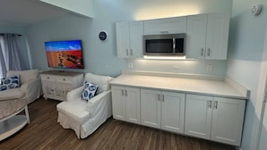 Espaço compacto com cozinha compacta, televisão de tela plana e área de jantar com mesa e cadeiras brancas.