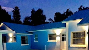 A swimming pool with a metal ladder, surrounded by a brick patio, and adjacent to a building with a blue exterior and multiple windows. - Walk to Beach, Siesta Key Villa 2, Pool View. Daily Rentals (Sarasota)