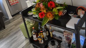 Una habitación con televisión mostrando un campo de golf, una zona de bar con un centro de mesa floral y una cocina al fondo.