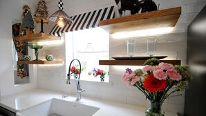 Una cocina moderna con encimeras blancas, un lavamanos de acero inoxidable, estantes de madera y un jarrón con flores.
