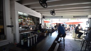 Una zona de bar con una barra larga, estantes con botellas y taburetes.