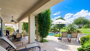Un patio exterior con piscina, sillones de descanso y una mesa con sillas.
