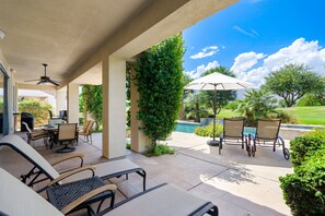 Patio esterno con piscina, poltrona relax e tavolo con sedie.