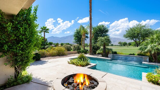 Un área de piscina con una chimenea, rodeada de follaje y vistas a las montañas.