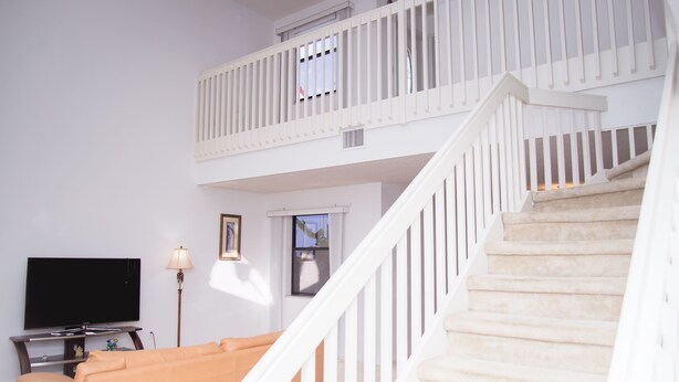 Una sala de estar con televisión, sofá, lámpara y una escalera.