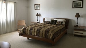 Un dormitorio con una cama, dos mesitas de noche, una silla, un ventilador de techo y dos cuadros enmarcados en la pared.