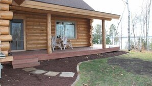 A log cabin with a porch, two chairs, and a view of a lake. - Special Labor Day Weekend! The cabin is available for 6-8 guests in 3 bedrooms. (Longville)