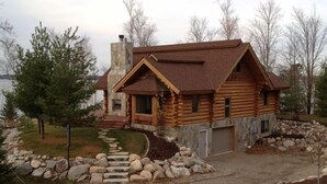 A log cabin with a stone chimney, a stone staircase leading to the entrance, and a stone retaining wall with rocks. - Special Labor Day Weekend! The cabin is available for 6-8 guests in 3 bedrooms. (Longville)