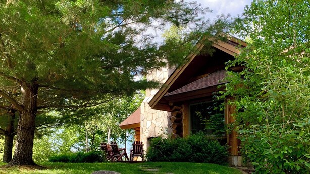 A stone staircase leading to a lodge with a stone exterior and a wooden roof, surrounded by lush greenery and trees. - Special Labor Day Weekend! The cabin is available for 6-8 guests in 3 bedrooms. (Longville)