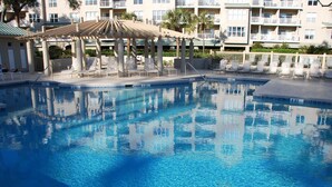 A swimming pool with lounge chairs and a covered seating area, surrounded by a multi-story building with balconies.