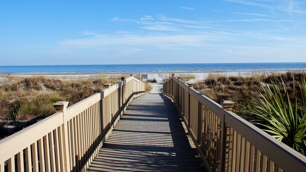 A wooden boardwalk leading to a beach with dunes and a clear sky.