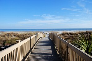 A wooden boardwalk leading to a beach with dunes and a clear sky.