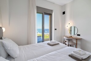 Une chambre d’hôtel avec un lit, un bureau, une chaise, un miroir et une vue sur la mer.