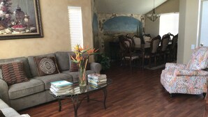 Ein Wohnzimmer mit Sofa, Sessel und Couchtisch. Im Hintergrund ist ein Essbereich mit Stühlen und Tisch zu sehen.