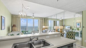 A modern kitchen with a double sink, a dishwasher, and a view of the ocean through large windows. - 1 Bedroom Beachfront Condo Sleeps 6 (Destin)