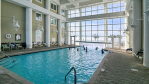 An indoor swimming pool with clear views of the sky through large windows, surrounded by columns and lounge chairs. - 1 Bedroom Beachfront Condo Sleeps 6 (Destin)