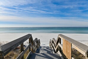 Un escalier en bois menant à une plage, avec un ciel dégagé.